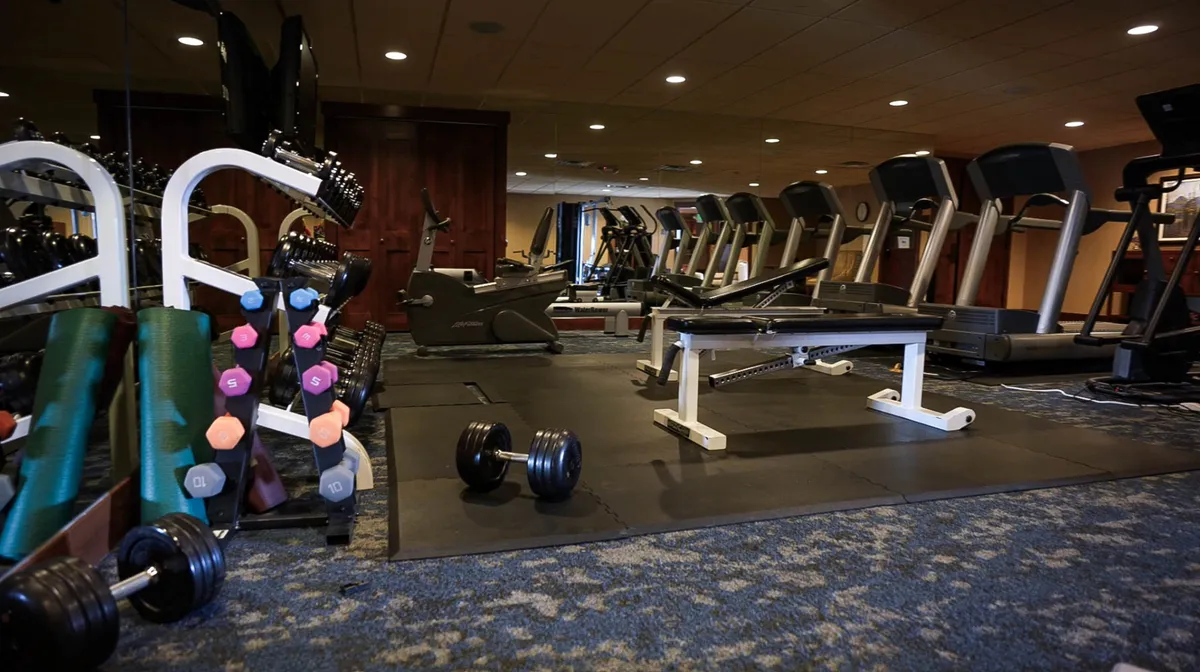 A modern fitness center featuring rows of dumbbells, treadmills, and an exercise bench. The space is spacious and well-lit, creating an energetic and motivational environment for guests looking to exercise or de-stress after work.