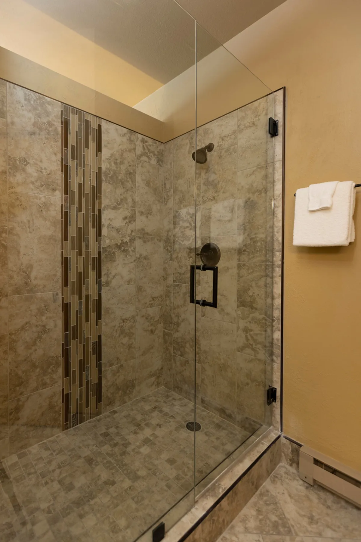 A modern bathroom featuring a glass shower enclosure, stylish fixtures, and a decorative tile strip. The space feels serene and rejuvenating, inviting guests to refresh and unwind in privacy.