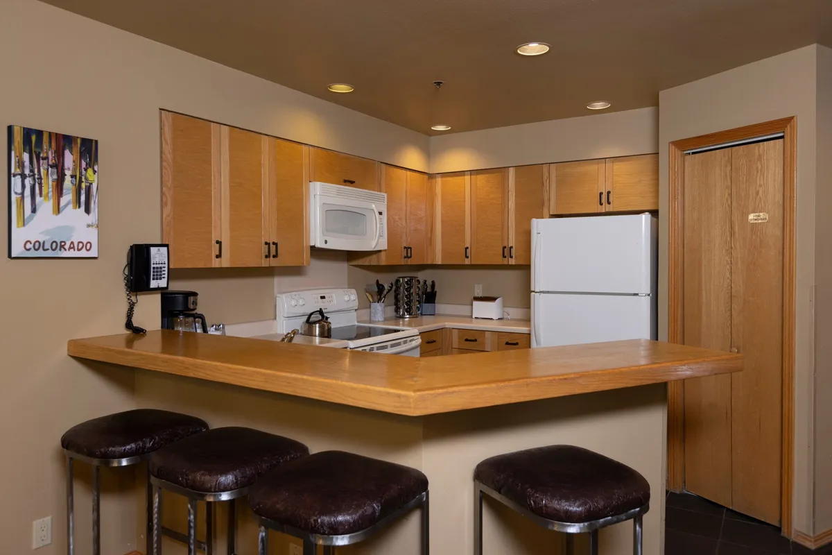 A cozy, functional kitchen featuring a spacious island with stools, modern appliances, ample cabinetry, and warm lighting. The space is open, inviting, and clearly supports both cooking and socializing, with room for guests to gather around the island.