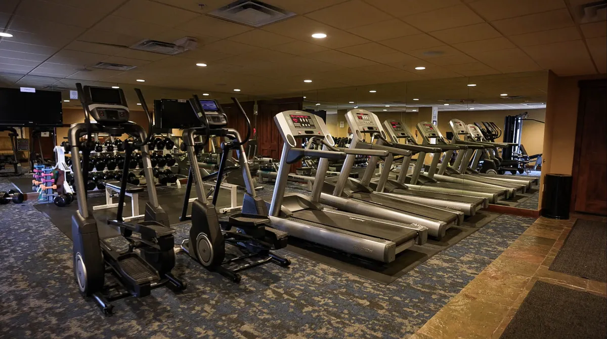 A modern fitness center filled with cardio machines, dumbbells, mirrors, and exercise mats. The atmosphere is vibrant and energetic, with space for both solo and group workouts.