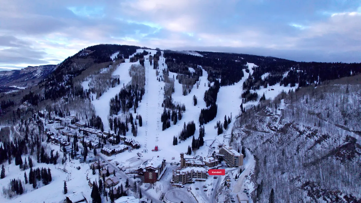 This viewpoint captures snow-dusted ski slopes, pine trees, and resort buildings nestled in a cozy mountain environment. The scene suggests a blend of adventure and relaxation, with ample opportunities for skiing, snowboarding, and après-ski gatherings. The backdrop further enhances the sense of a picturesque mountain escape.