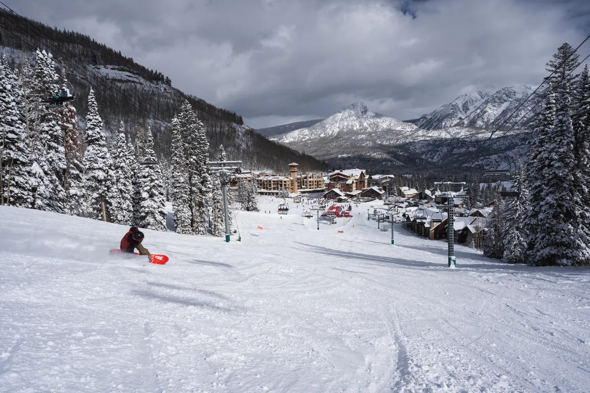 This image captures snow-covered slopes dotted with skiers and snowboarders, ski lifts ascending the mountainside, and resort buildings nestled below. The distant peaks and expanse of snow convey the thrill and beauty of winter sports right outside the property.