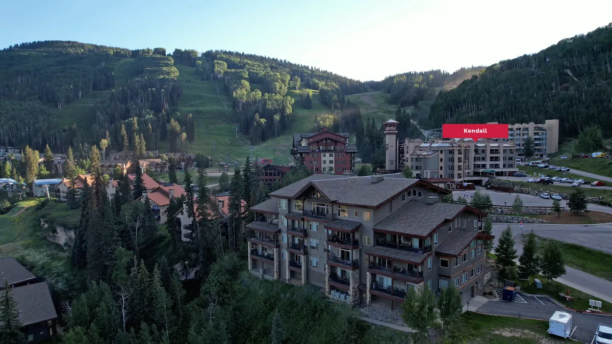 Resort buildings are framed by a mountain backdrop and a tree-lined area, with hints of outdoor dining and relaxation spaces. The tranquil setting invites families to gather, take in the views, and enjoy the outdoors together.