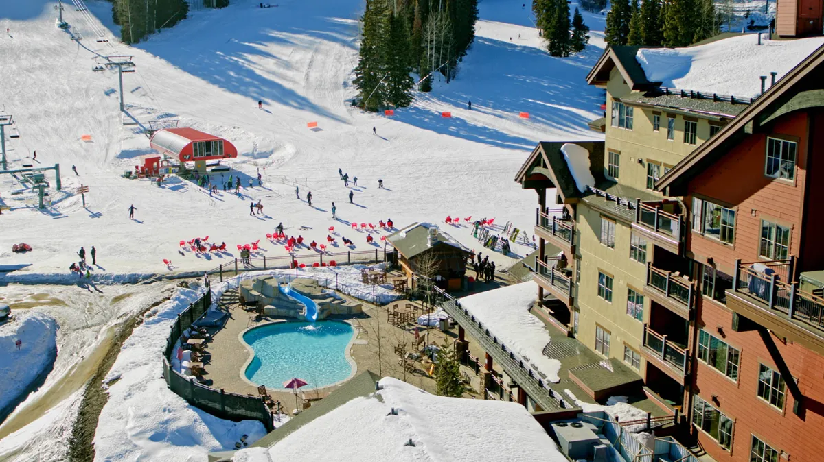 A lively scene featuring a heated swimming pool set against a backdrop of ski slopes, a ski lift, and a cozy lodge. People enjoy both swimming and winter sports, emphasizing the blend of recreation and relaxation.