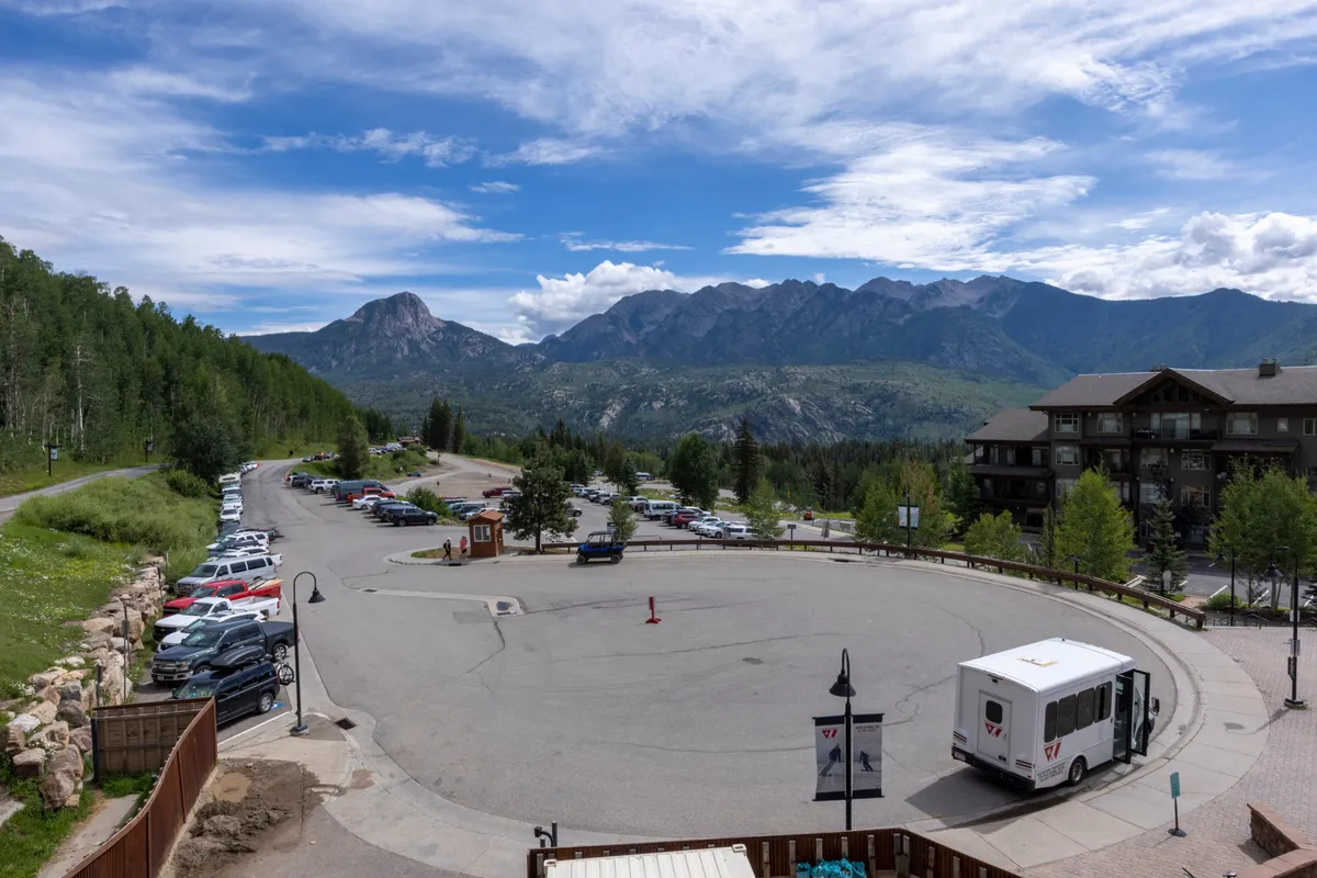 A welcoming exterior scene featuring a pathway leading from the parking area toward a lodge, with expansive mountain views in the distance. The setting hints at hiking opportunities and outdoor gatherings, with a sense of adventure embedded in the natural landscape.